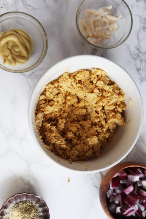 Mashed chickpeas in a white bowl for a chickpea salad sandwich by Naturally Tessa